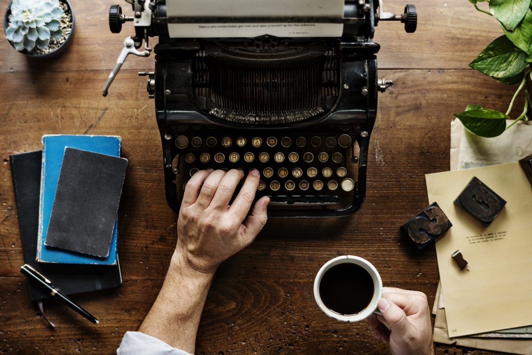 A person holding a cup of coffee while typing on a retro typewriter